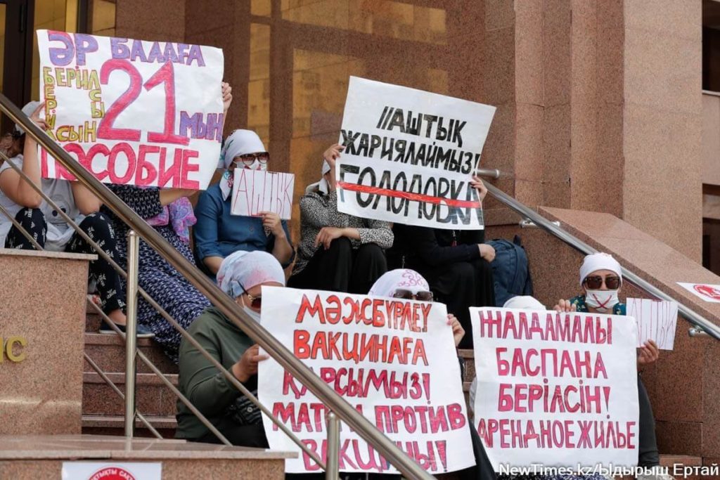 In Kazakhstan, mothers with large signs demonstrate by sitting on the steps of a building. They want adequate housing and child benefits.