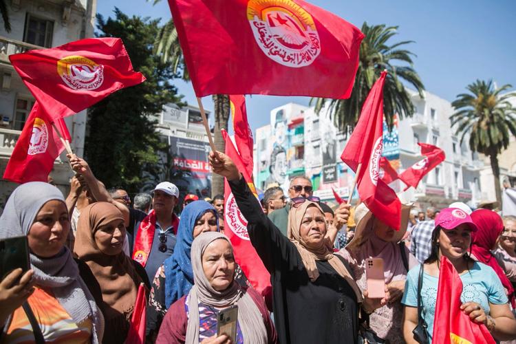 Tunisian women in colorful scarves wave flags as they protest against austerity measures.