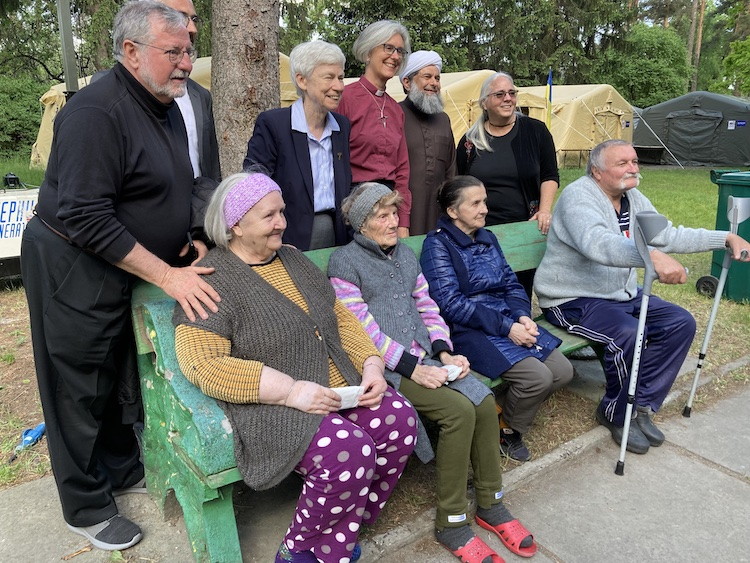 Six members of an international, interfaith peace team meet with residents of Kyiv, Ukraine, in a public park. Tent shelters have been set up behind them.