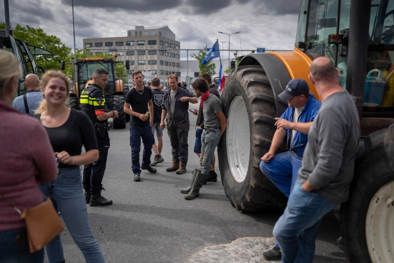 A group of 9 Dutch farmers stand next to large tractors in the streets of a city where they are protesting rules on nitrogen emissions that threaten to put them out of business.