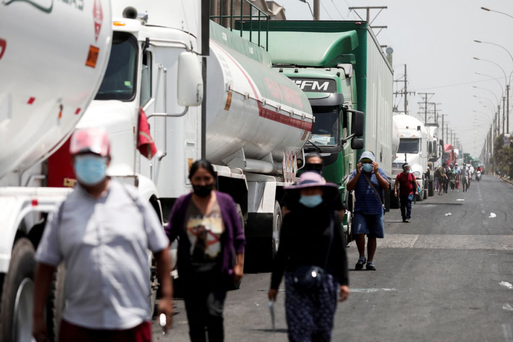 People walk next to parked semi-trucks during a truckers strike against high fuel prices in Lima, Peru.