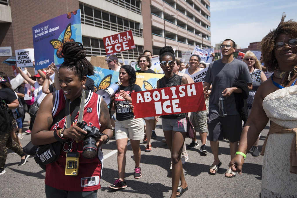 People carry red and white signs saying "abolish ICE" as they march down a street near a migrant detention center in New Jersey.