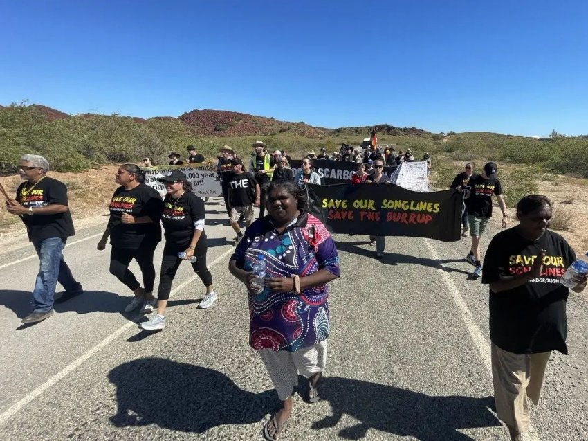 Aboriginal Australians march down a road carrying banners and signs opposing a gas processing plant.