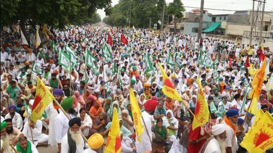 Over a hundred Indian farmers in white clothes hold flags and sit in the road in protest of lack of water.