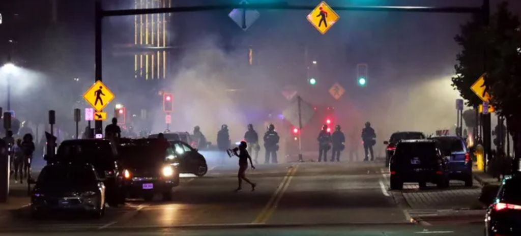 At night, a line of police and tear gas meet protesters objecting to the murder of Jayland Walker in Akron, OH.
