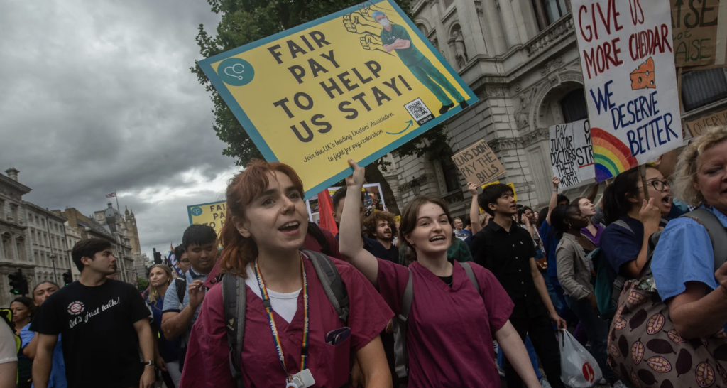 Nurses in scrubs protest with hundreds more. They are part of the United Kingdom's Hot  Strike Summer with 200,000 workers from many sectors on strike.