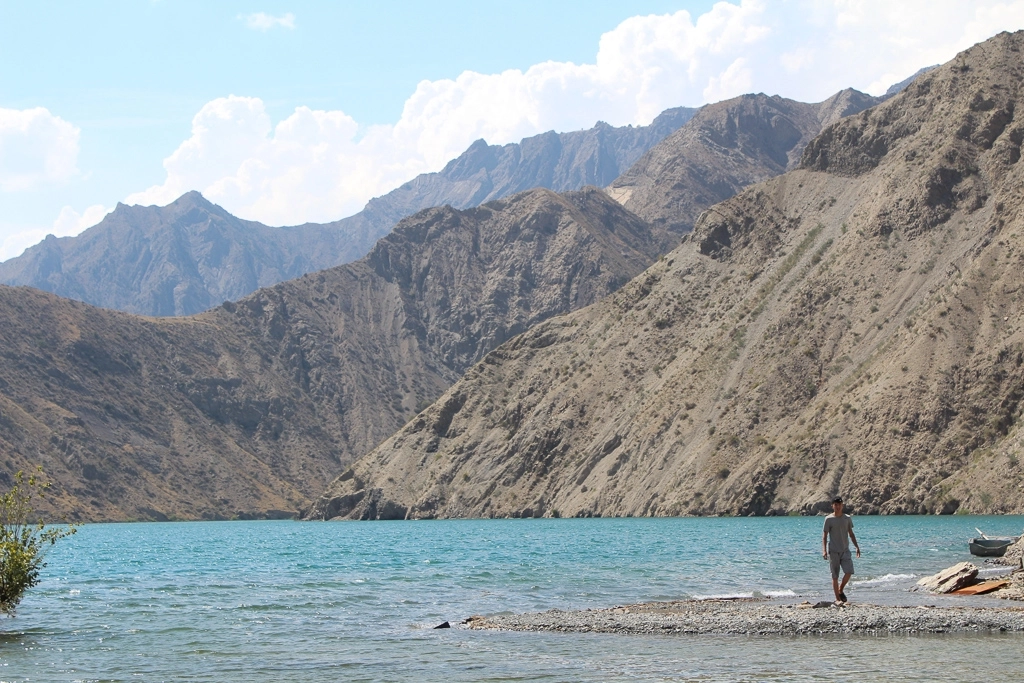 In Kyrgyzstan, a man walks along side a vivid blue lake near steep mountains that are threatened by a mine.
