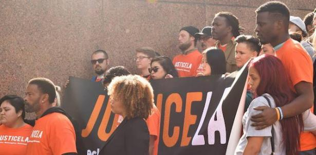 Campaigners with JusticeLA wear orange shirts and stand together, demonstrating to abolish prisons.