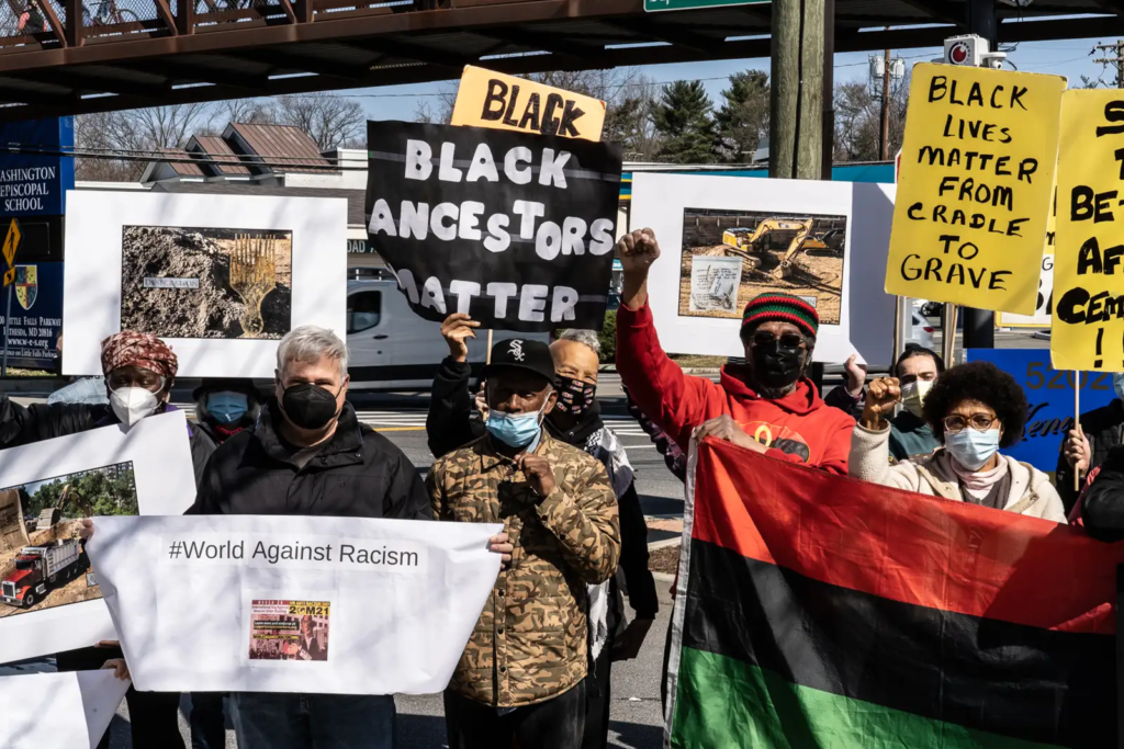 A group of Black Americans and allies hold Black Lives Matter and Black Ancestors Matter signs has they demonstrate to protect a Black cemetery threatened by development.