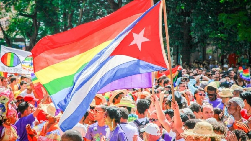A crowd of Cubans hold up a gay pride flag alongside the national flag at an LGBTQ rally.