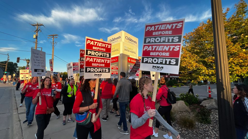 Michigan nurses form a picket line during their recent, successful strike. They wear bright red shirts and hold signs that say "patients before profits".