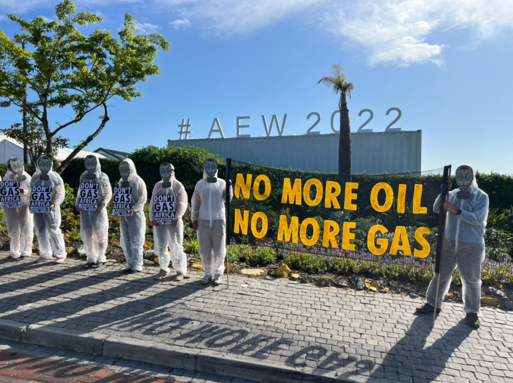 Dressed in white hazmat suits, a group of climate protesters wearing gas masks over their faces hold signs and banners opposing oil and gas extraction in South Africa. 