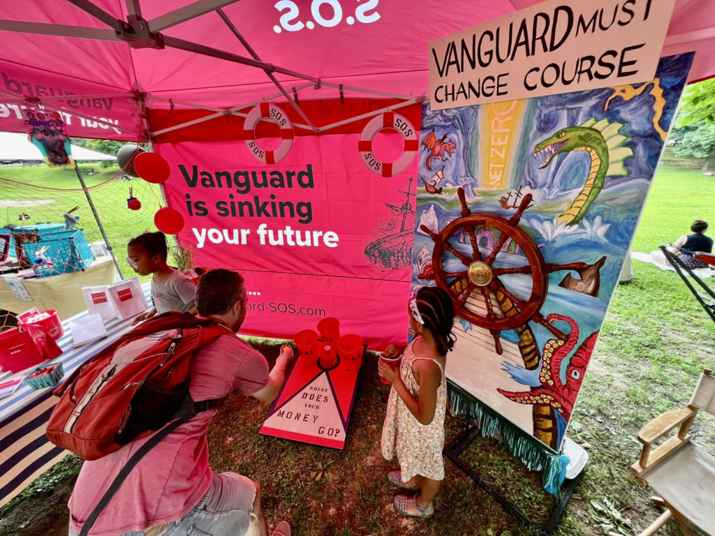 A father and daughter play a game in a pink pop-up tent booth that teaches families how the investment company Vanguard isn't climate-friendly.