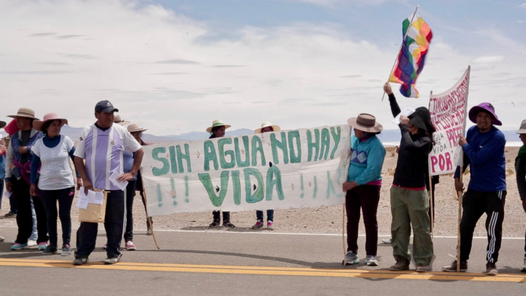 A small group of Indigenous Argentines protest against a lithium mine. They carry a banner that reads "without water there is no life" in Spanish.