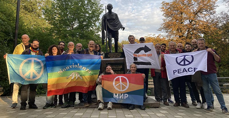 Holding five colorful flags for peace in multiple languages, members of a peace delegation to Ukraine stand by the Gandhi statues in Kyiv.