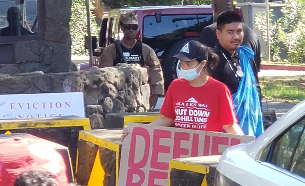 Several Hawai'ians hold protest signs as they stand at the gates of a US navy base that contaminated the water. 