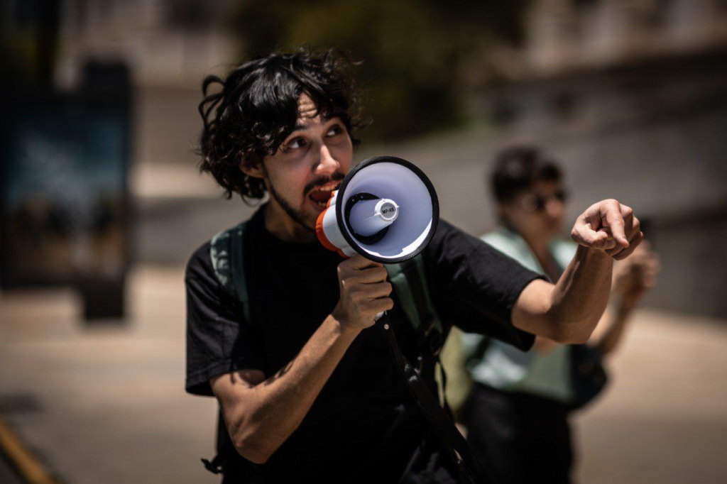 A climate activist in Argentina decries ecocide. He holds a megaphone and gestures in frustration.