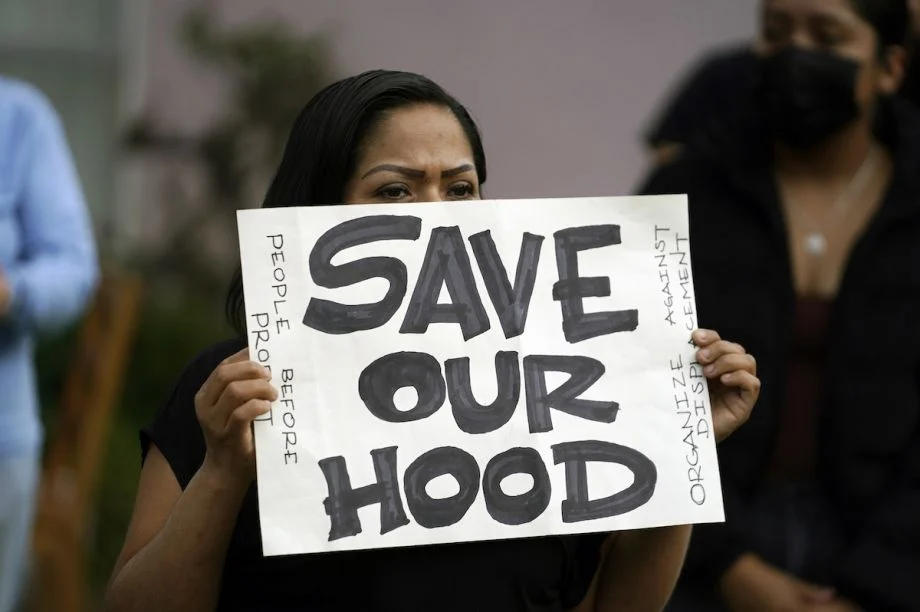 A tenant holds a sign reading “Save Our Hood,” at a community rally in the Baldwin Hills neighborhood urging Boston University officials not to sell their buildings to investors in Los Angeles.