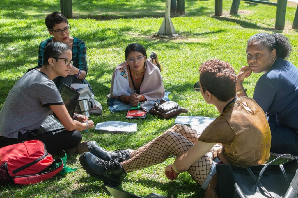 A group of Central American women sit in a circle on the grass in deep discussion.