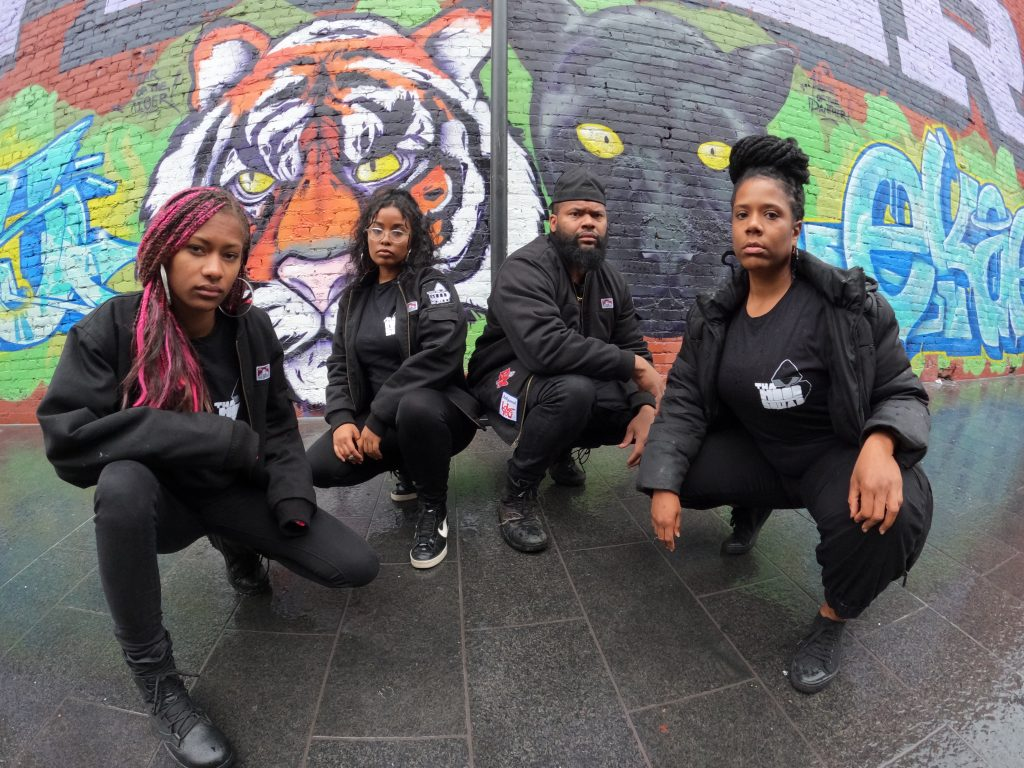 Four Black activists in Oakland, CA, strike a pose in front of a graffiti mural of a tiger and a panther.