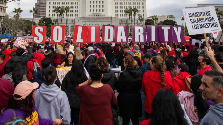 A demonstration of teachers hold up red and purple letter signs that spell out solidarity.