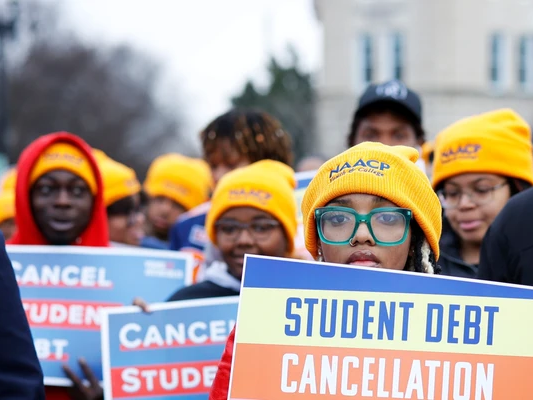 Wearing bright yellow ski hats, a group of students holds signs calling for student debt cancellation as they rally in front of the US Supreme Court.