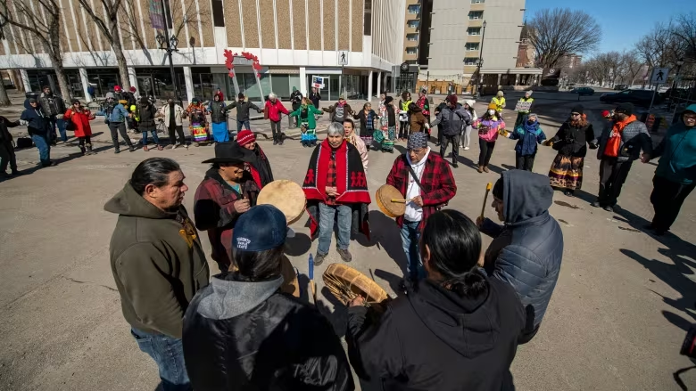 A circle of Indigenous drummers is surrounded by supporters holding hands during a protest against fossil fuel financing in Saskatoon, Canada.
